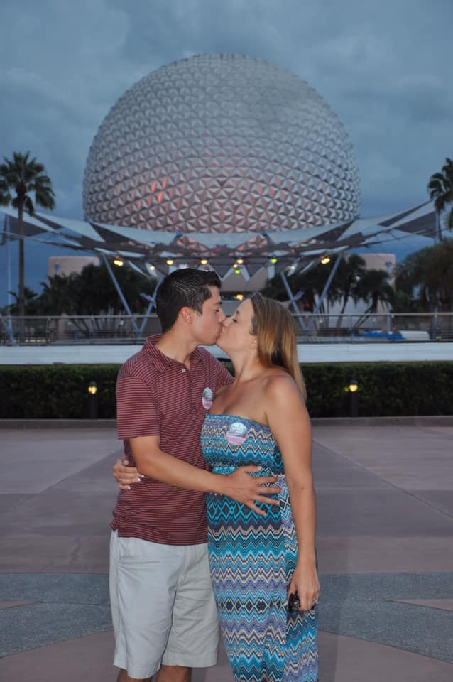 A man and woman kissing in front of the spaceship earth.