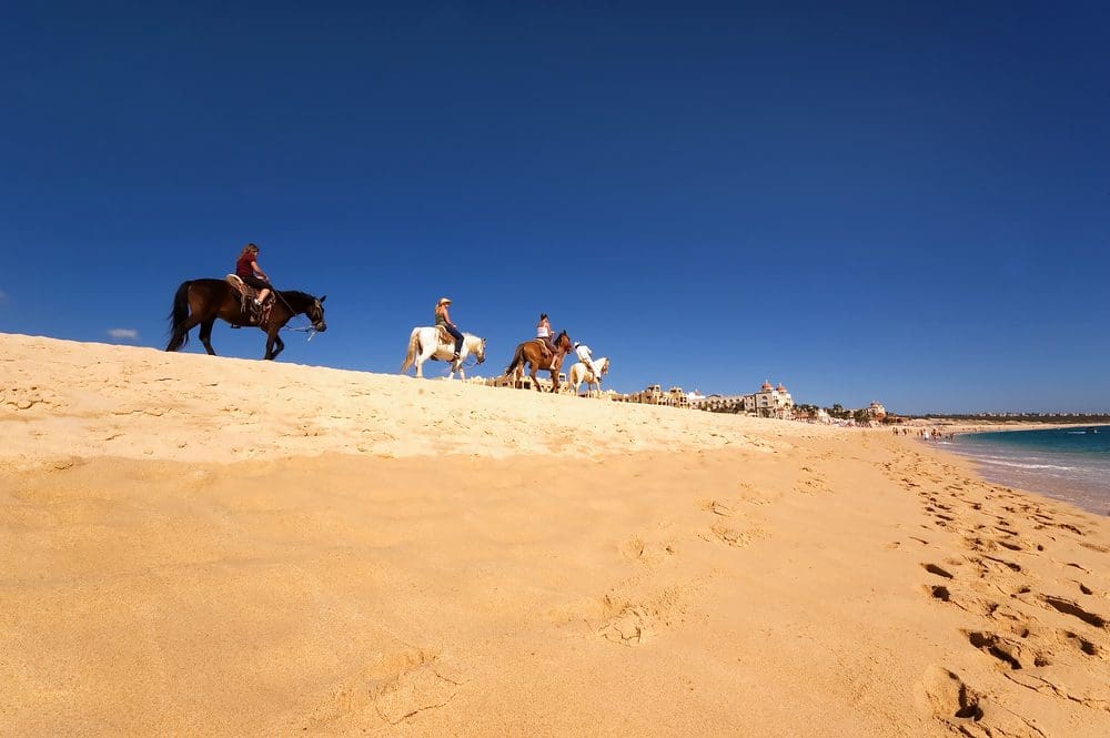 A group of people riding horses on top of a sandy hill.