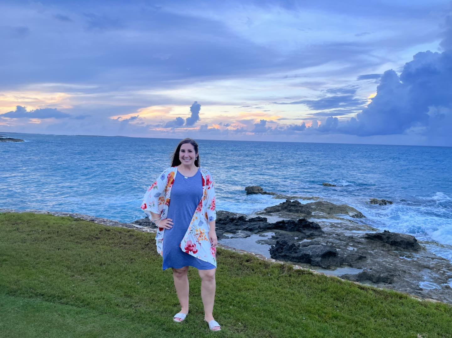 A woman standing on the grass near the ocean.