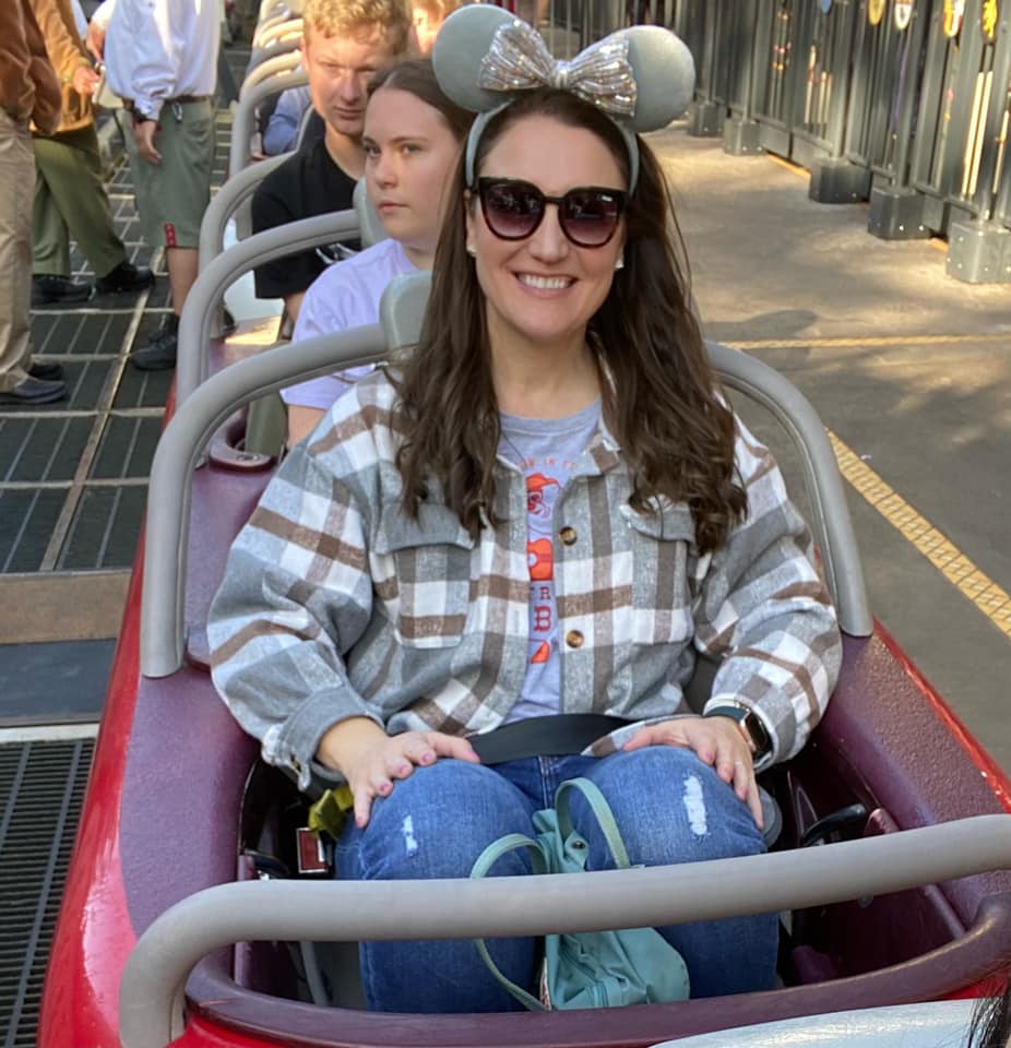 A woman in plaid shirt riding on a red roller coaster.