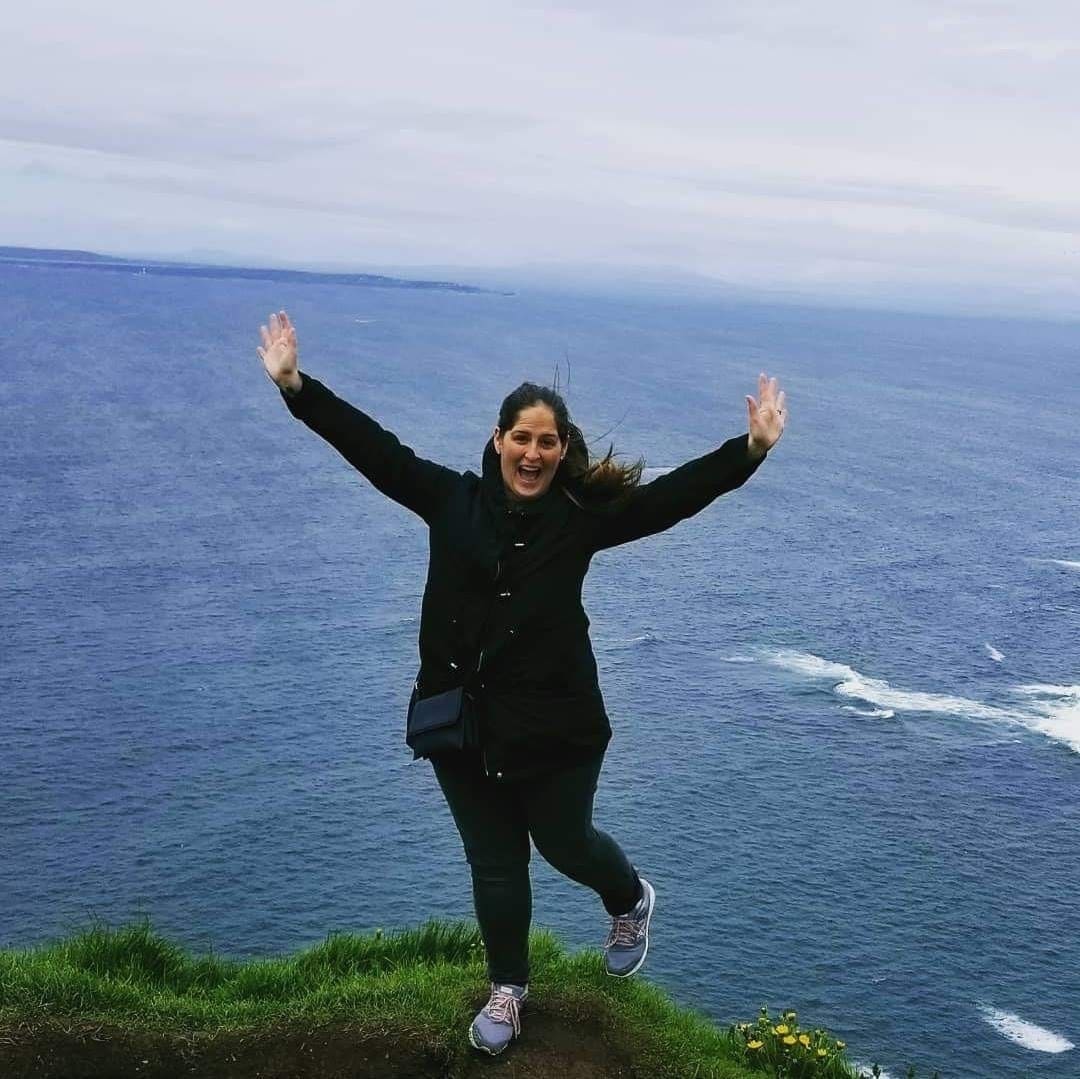 A woman standing on top of a hill near the ocean.