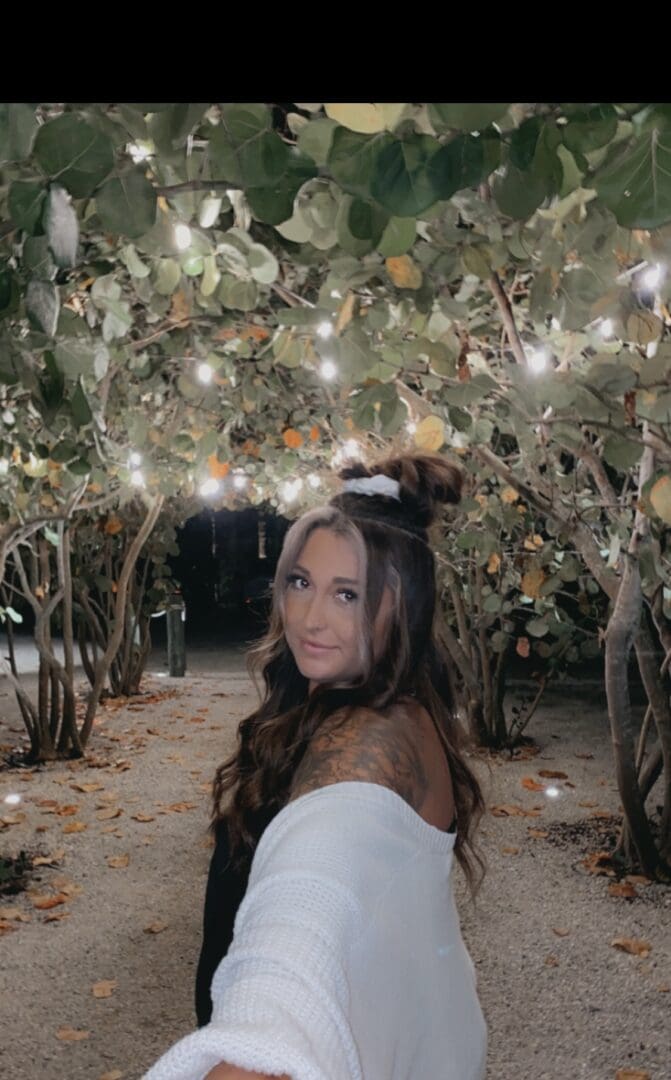 A woman in white dress standing under trees.