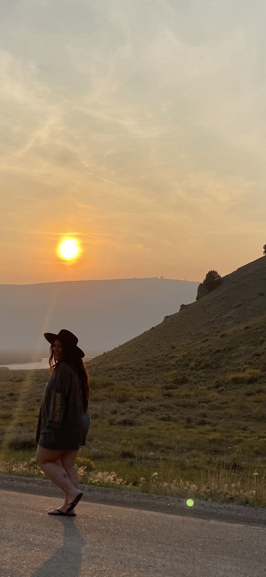 A woman standing on top of a hill near the sun.