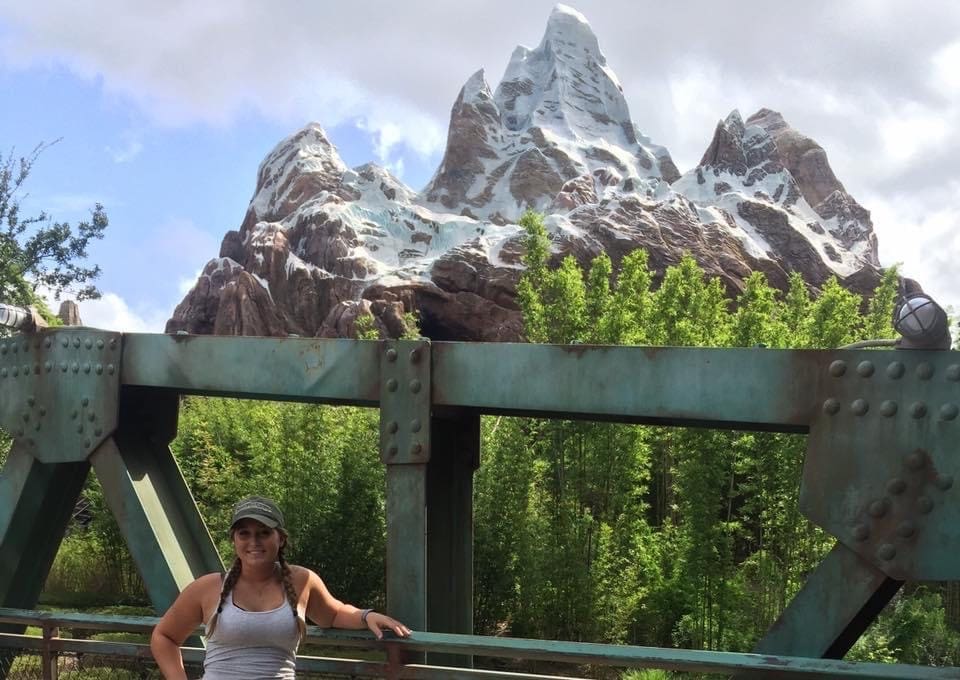 A woman standing on the side of a bridge near some trees.