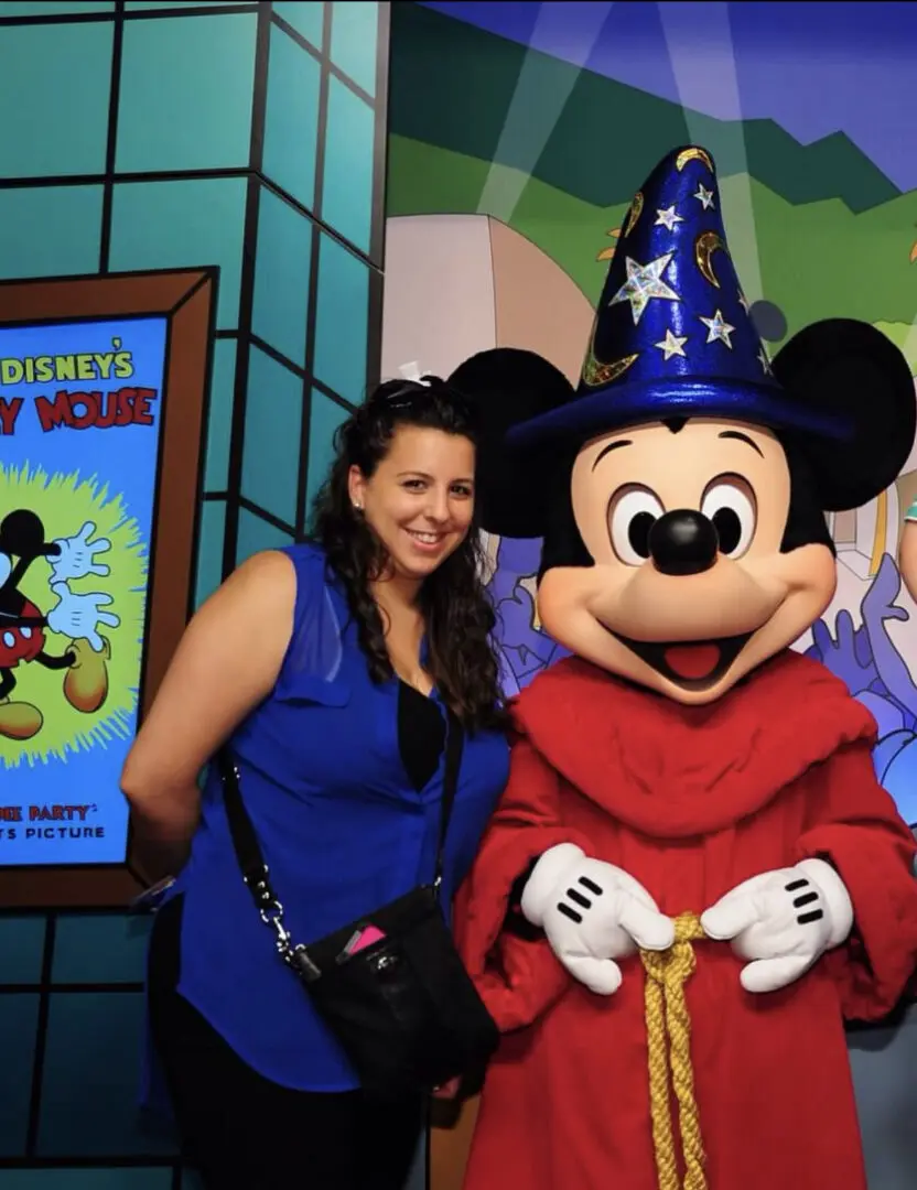 A woman posing with mickey mouse in front of a poster.