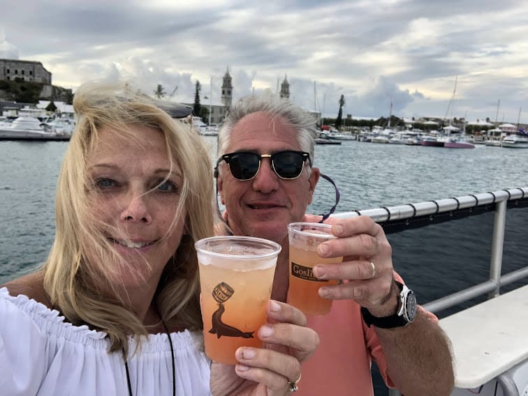 A man and woman holding drinks on the deck of a boat.