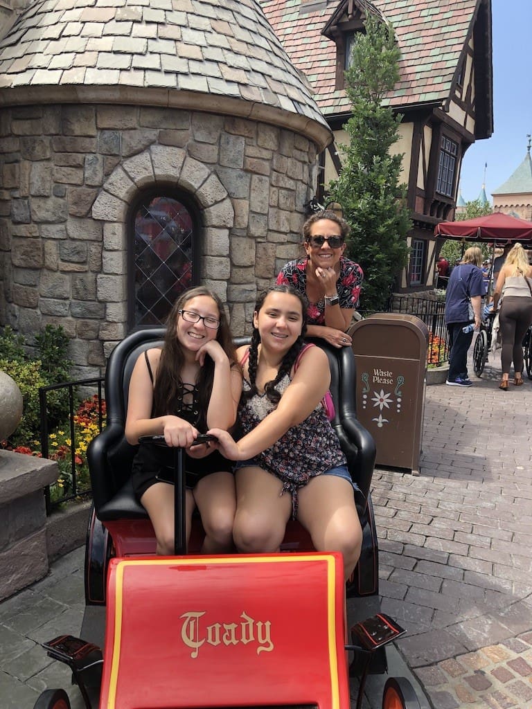 Three girls sitting on a carriage in front of a castle.