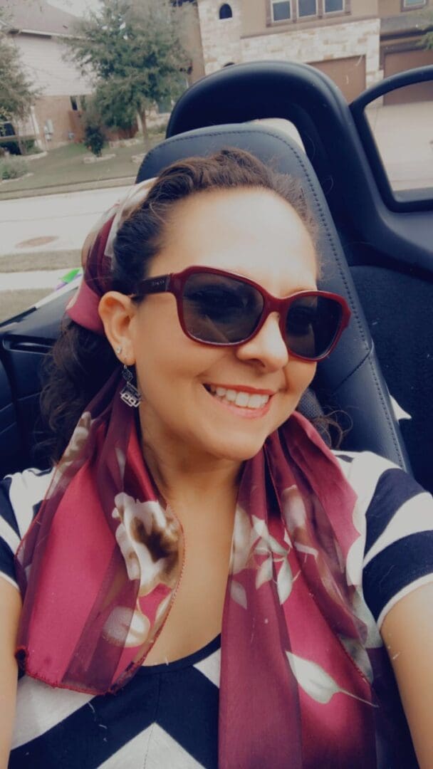 A woman in sunglasses and scarf sitting in the back of a car.