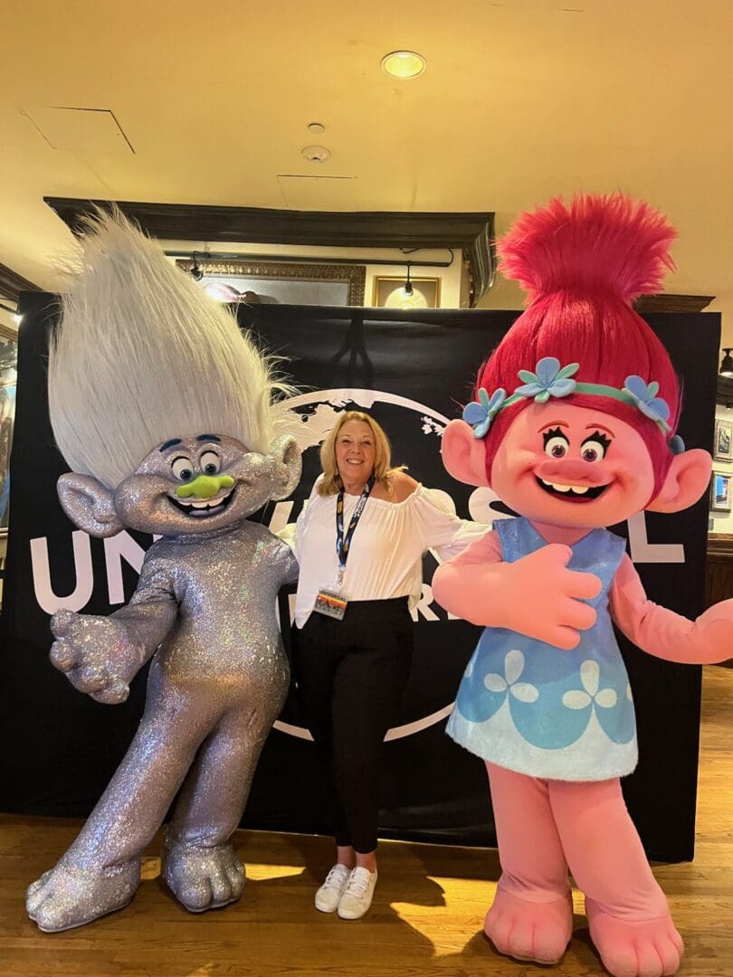 A woman standing next to two trolls in front of a sign.