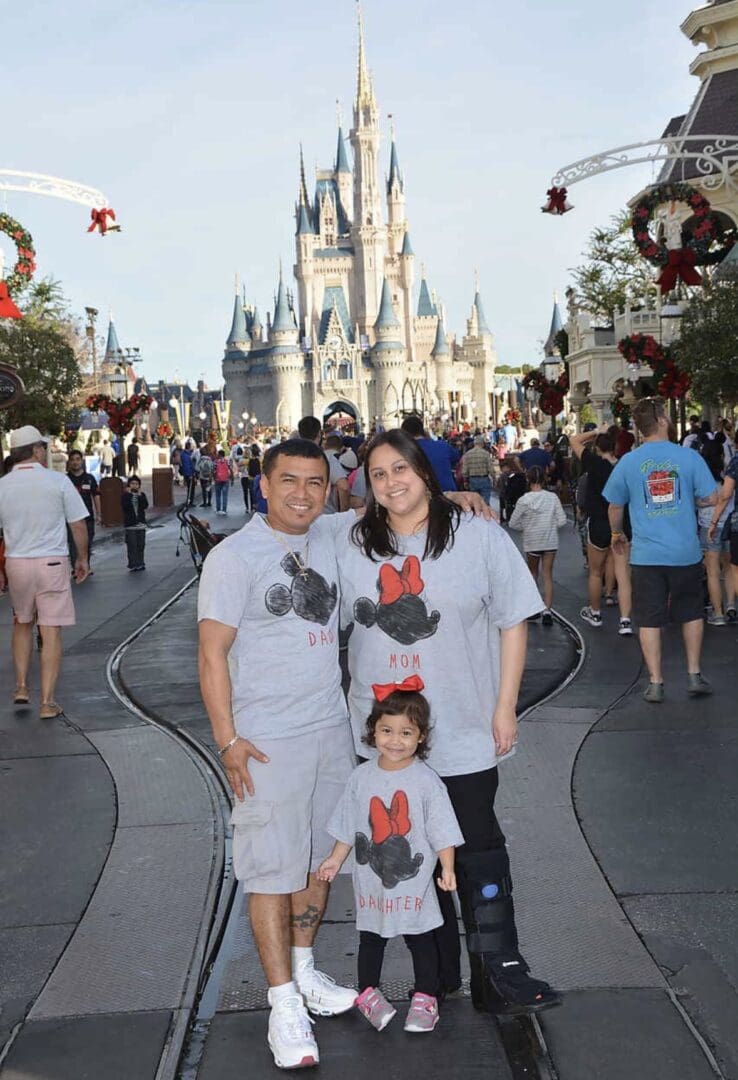 A family of three posing for the camera in front of a castle.