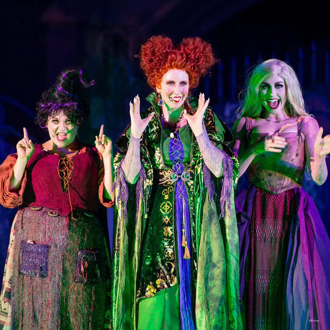 Three witches in Halloween costumes on stage.