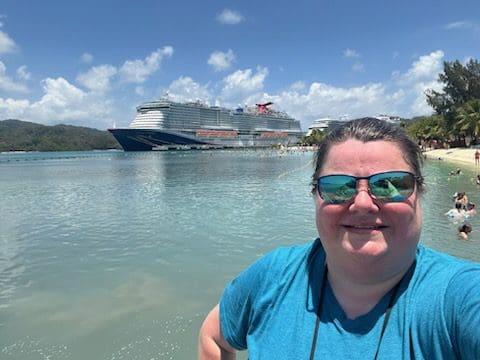 Woman in sunglasses with cruise ship in background.