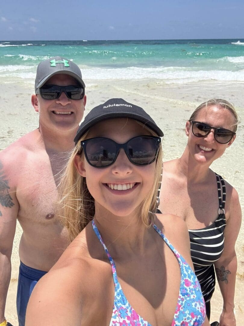Three people smiling on a sunny beach.