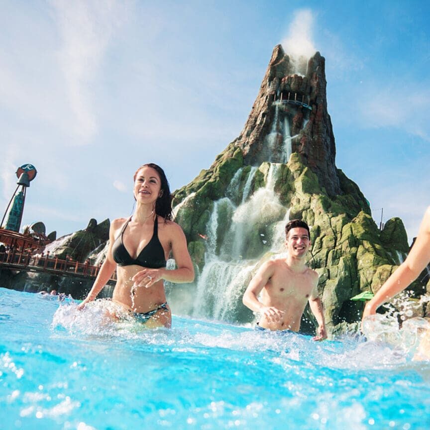 People enjoying water park with volcano backdrop.